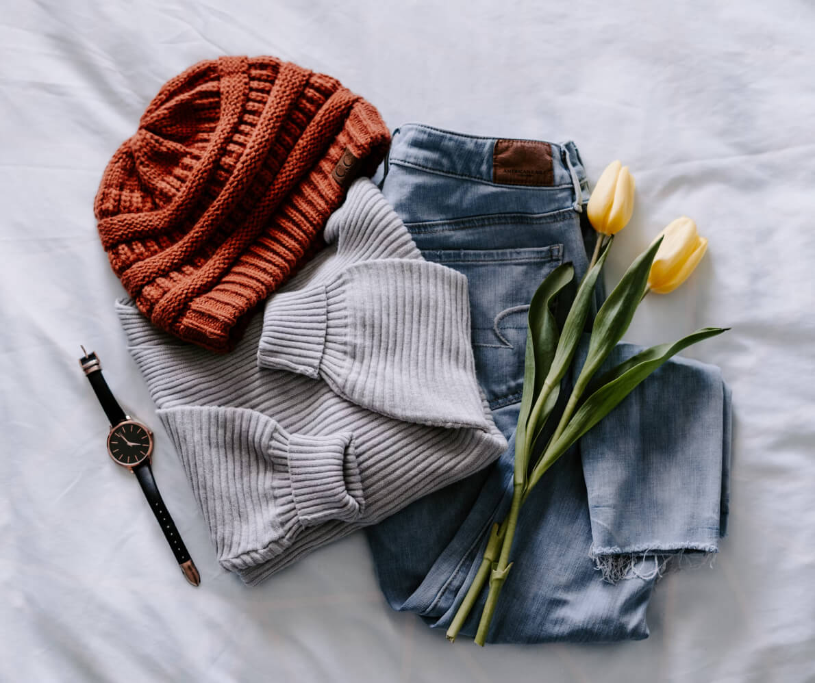 A pair of jeans, a sweater, and a tulip on a bed.